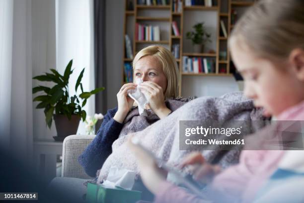 mother sitting on couch, having a cold, daughter playing in foreground - woman home with sick children imagens e fotografias de stock