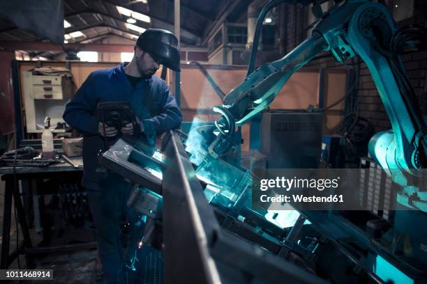 welder welding metal with robot - worker inspecting steel foto e immagini stock