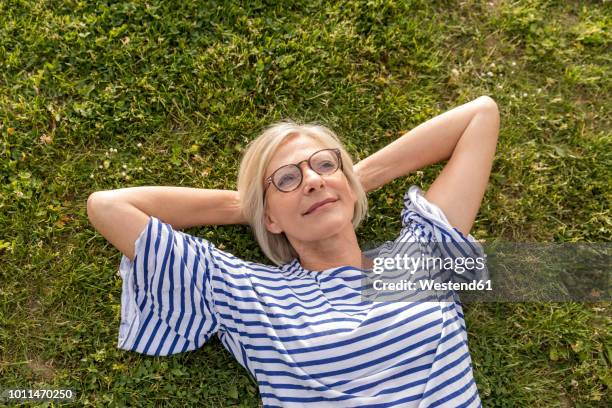 portrait of smiling senior woman lying in grass - women lying stock-fotos und bilder