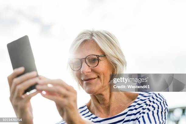 smiling senior woman using cell phone outdoors - relaxed sunshine happy lens flare stock pictures, royalty-free photos & images