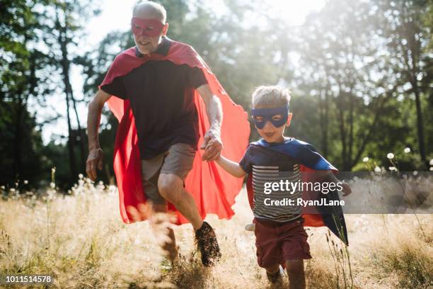 großvater, verkleidet als superheld spielt draußen mit enkel - child playing dress up stock-fotos und bilder