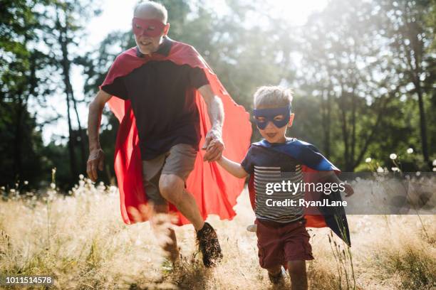 grandfather dressed as superhero plays outside with grandson - heróis imagens e fotografias de stock