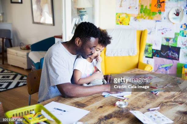 Father and toddler daughter coloring at table