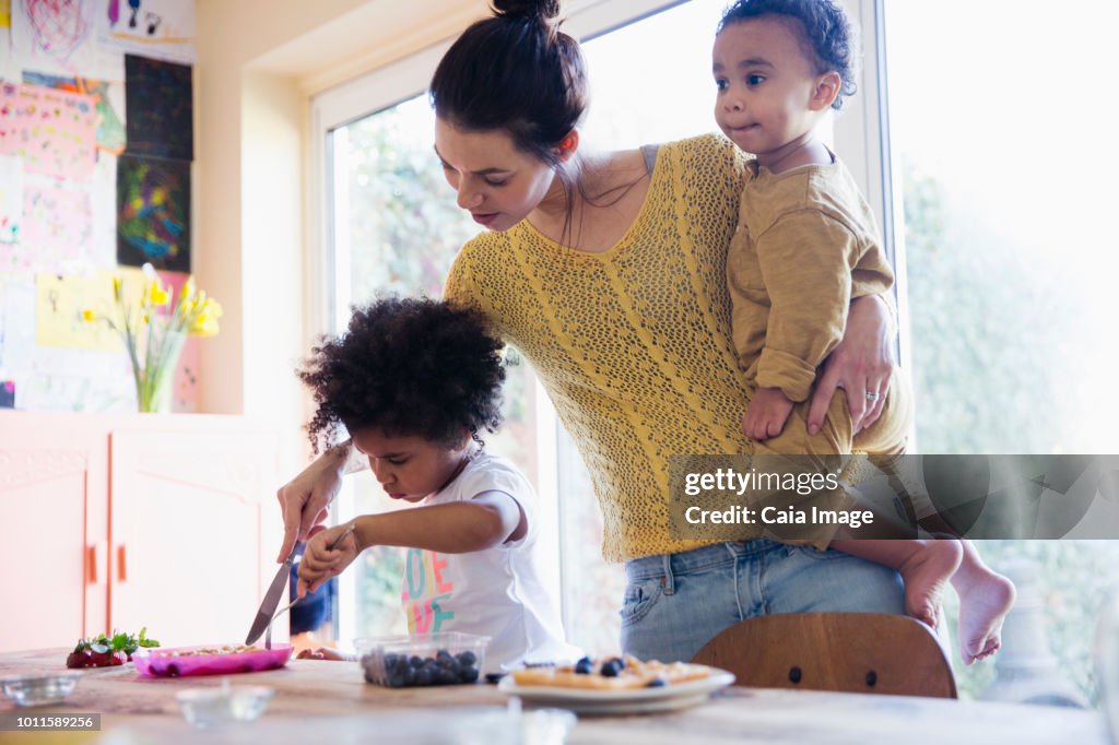 Mother helping toddler daughter cutting breakfast waffles