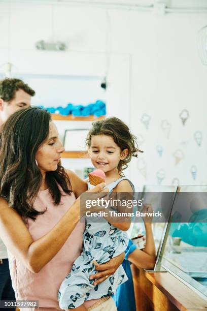 mother holding smiling daughter while handing her ice cream cone in ice cream shop - ice cream parlour stock pictures, royalty-free photos & images