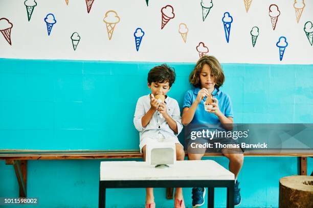 young brothers sitting in ice cream shop enjoying ice cream - ice cream parlour stock pictures, royalty-free photos & images