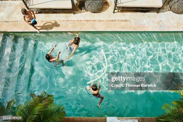 overhead view of family playing together in pool at tropical resort - リゾート　家族 ストックフォトと画像