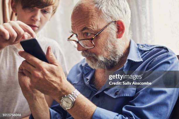 teenager using a smartphone with his grandfather - abuelos fotografías e imágenes de stock