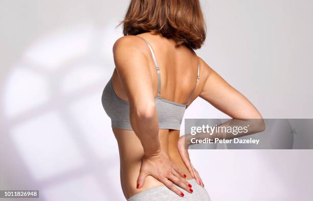 woman massaging her painful back due to sports injury - personal hygiene product stock pictures, royalty-free photos & images