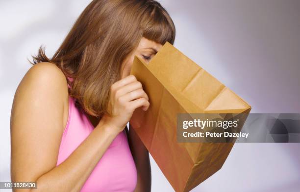 woman vomiting into paperbag - vomitare foto e immagini stock