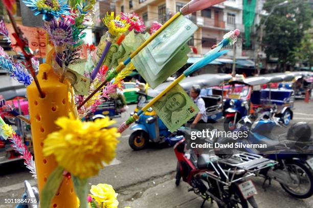 Offerings of banknotes and flowers adorn a pavement Buddhist shrine by the city's downtown produce market during Asahna Bucha celebrations on July...