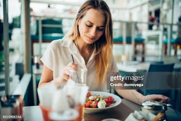 young woman sitting in a restaurant and eating mediterranean food - greek salad stock pictures, royalty-free photos & images