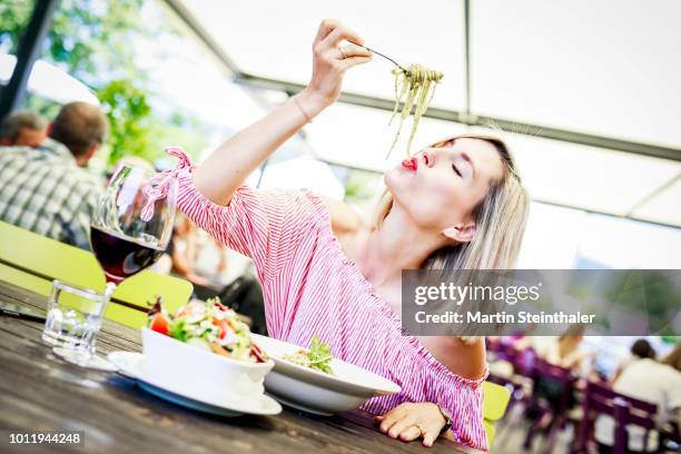 junge frau schlürft spaghetti in gastgarten - frau essen stock pictures, royalty-free photos & images