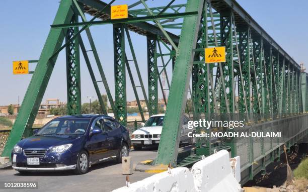 This picture taken on August 6 shows vehicles crossing the single-lane iron bridge in the Iraqi city of Fallujah, as it reopens after its destruction...