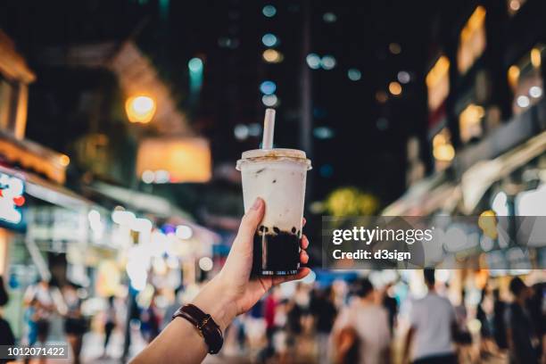 human hand holding a bottle of iced cold bubble tea against busy city street at night - hong kong street food stock pictures, royalty-free photos & images