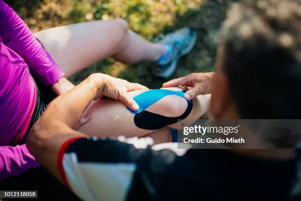 man applying bandage on knee of his wife. - sports injuries stock pictures, royalty-free photos & images