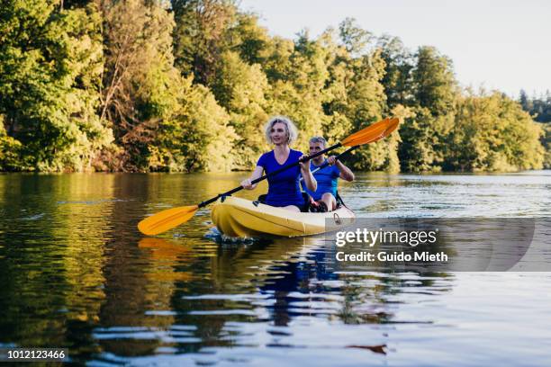 mature couple canoeing at a lake. - seniors canoeing stock pictures, royalty-free photos & images
