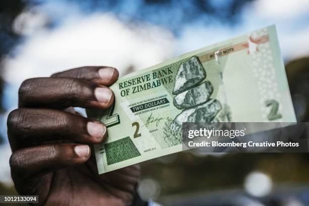 a man holds a zimbabwean two dollar bond banknote - zimbabwe fotografías e imágenes de stock