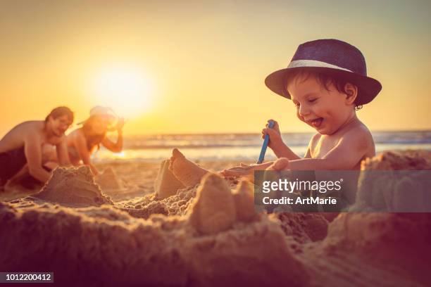 happy little boy building sandcastle on the beach - bucket and spade stock pictures, royalty-free photos & images
