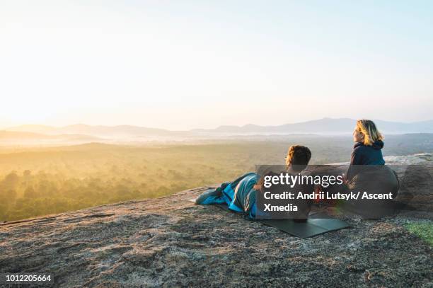 young couple relax on rocky crest above jungle, sunrise - couple paysage asie photos et images de collection