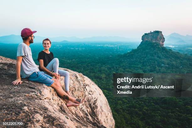 young couple relax on rocky crest above jungle, sunrise - tee srilanka stock pictures, royalty-free photos & images