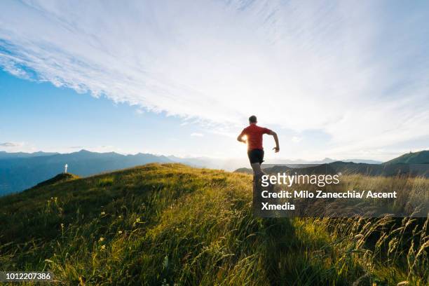 trail runner follows alpine track, on mountain ridge - gebirgskamm stock-fotos und bilder