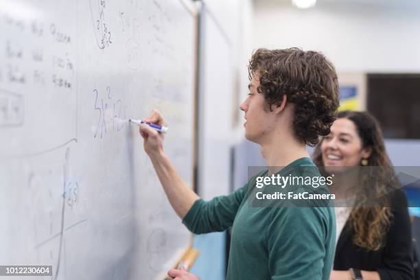 etnische leraar helpt middelbare schoolstudent met een wiskundige probleem op het whiteboard - wiskunde stockfoto's en -beelden