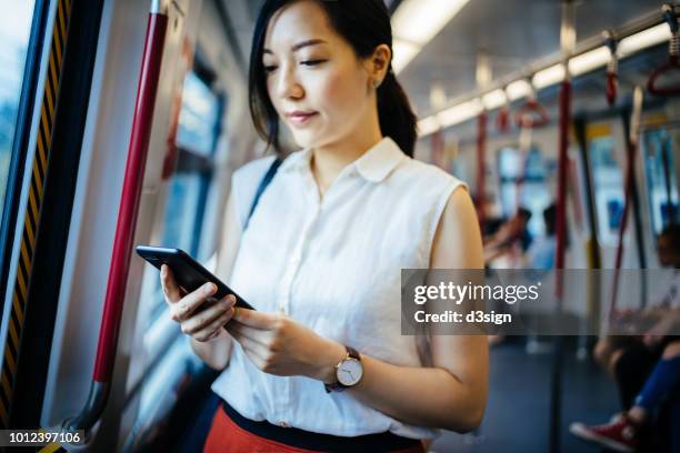 beautiful young lady text messaging on smartphone while riding on subway mtr train - hong kong mass transit fotografías e imágenes de stock