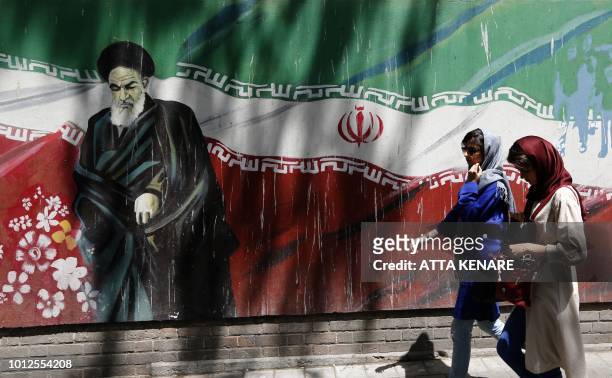 Iranians walk by mural painting of the founder of the Islamic Republic Ayatollah Ruhollah Khomeini on the wall of the former US embassy in the...