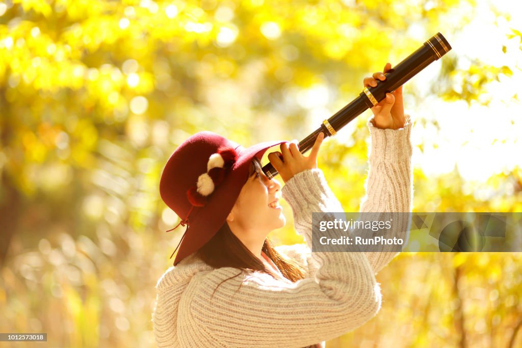Young woman looking through telescope in autumn park