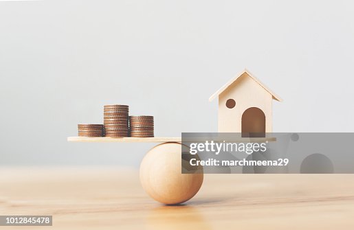 Wooden home and money coins stack on wood scale. Property investment and house mortgage financial real estate concept Wooden home and money coins stack on wood scale. Property investment and house mortgage financial real estate concept