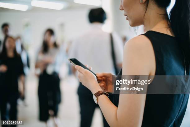 close up of young woman using mobile phone against busy commuters in city - crowded train station smartphone ストックフォトと画像