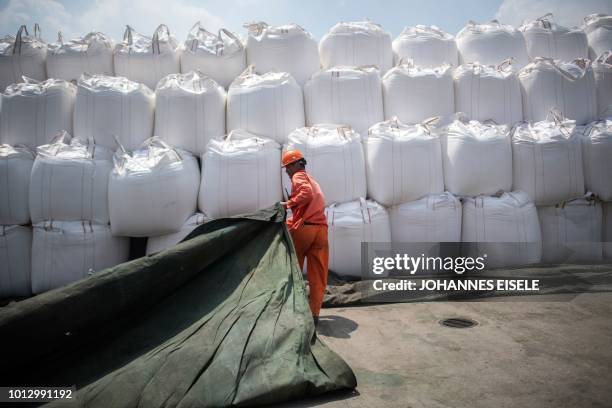 This photo taken on August 7, 2018 shows a worker covering bags of chemicals with a sheet at a port in Zhangjiagang in China's eastern Jiangsu...