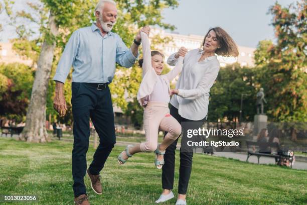 grandparents holding granddaughter by hand and lifting her up in the air - grandparents raising grandchildren stock pictures, royalty-free photos & images