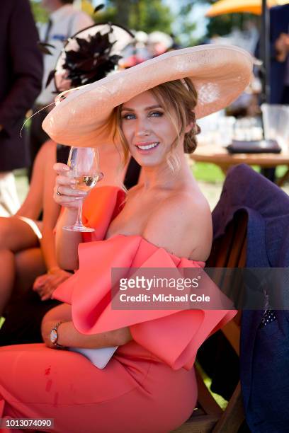Stylish racegoer wearing red dress and white hatinator, drinking champagne in the Veuve Clicquot area, 'Ladies Day' at "Glorious Goodwood" - The...