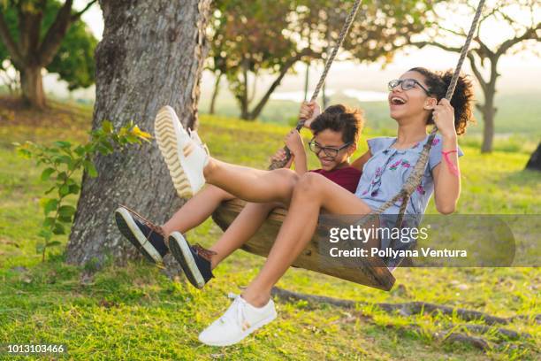 happy siblings playing on the swing - sibling stock pictures, royalty-free photos & images