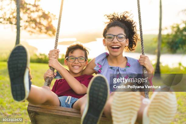glückliche kinder schwingen und lächeln an goldenen sonnenuntergang - season 13 stock-fotos und bilder