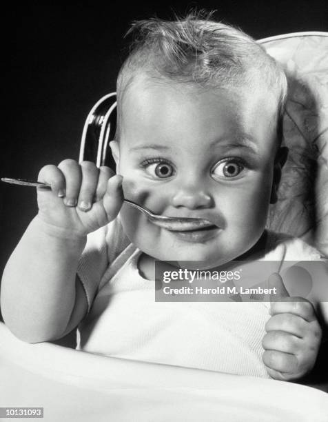 BABY IN HIGH CHAIR WITH SPOON TO MOUTH