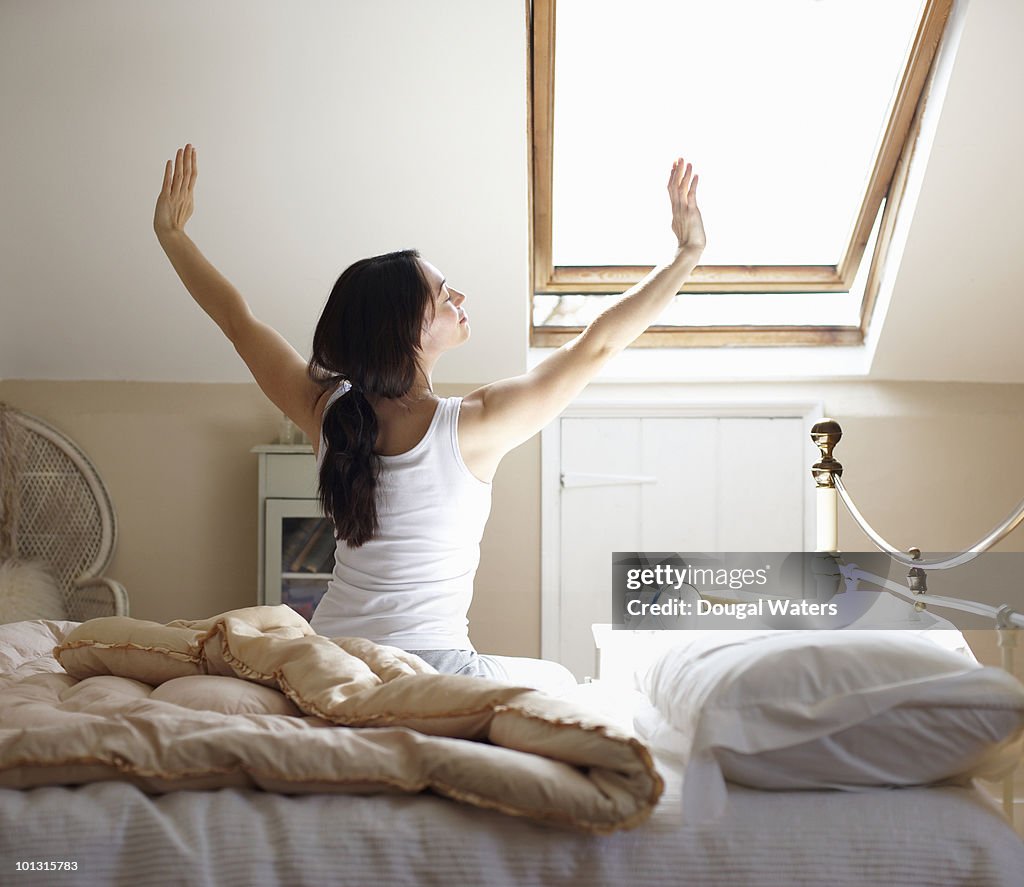 Woman stretching on edge of bed.