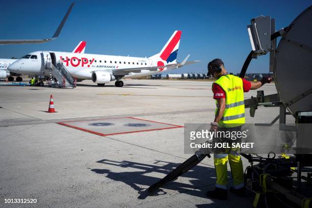 An employee prepares to refuel a plane as a Hop plane is parked on the tarmac of Roissy-Charles de Gaulle Airport, north of Paris, on August 6, 2018.
