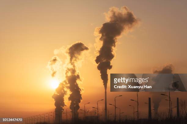 silhouette of a high industrial pipe with the sun behind it - ozonschicht stock-fotos und bilder