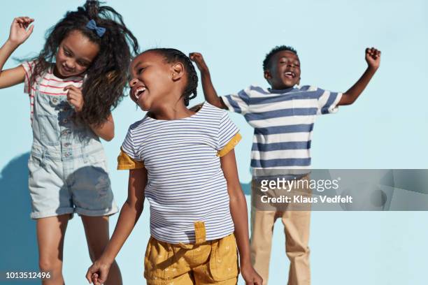 portrait of kids hanging out & playing together on blue backdrop in sunlight - child dancing stock pictures, royalty-free photos & images