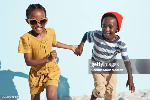 portrait of boy & girl holding hands and running, on blue backdrop in summer - kids fashion stock-fotos und bilder