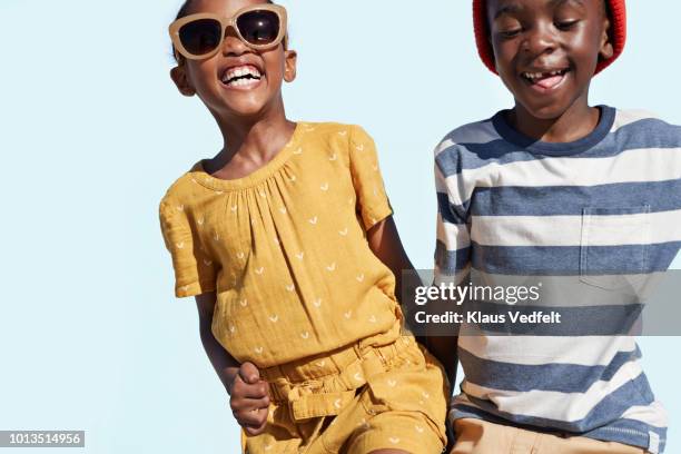 portrait of boy & girl holding hands and laughing, on blue backdrop in summer - fashion kids stock pictures, royalty-free photos & images