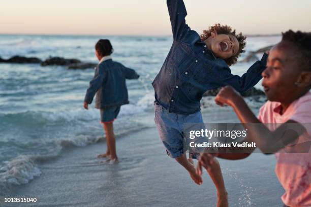 kids jumping in the water's edge at sunset - jumping into water stock pictures, royalty-free photos & images