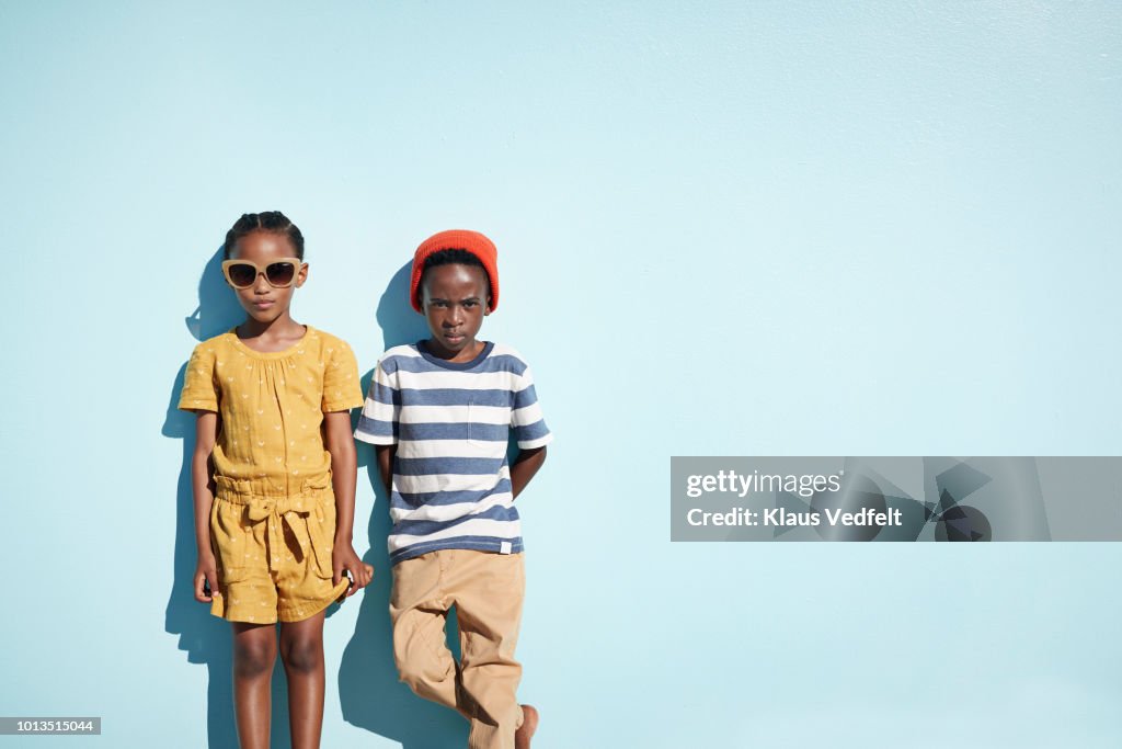 Portrait of boy & girl holding hands and looking in camera, on blue backdrop in summer