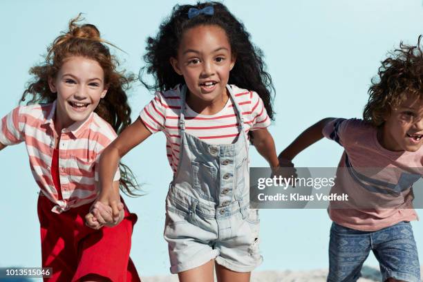 portrait of kids holding hands and running together, on blue backdrop in summer - pink shorts stock-fotos und bilder