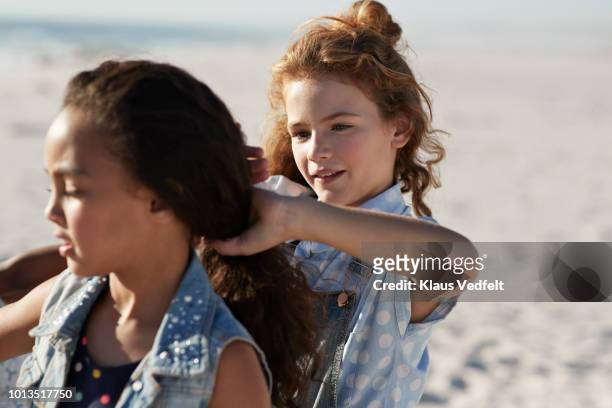cute girls braiding each others hair, on the beach - girl hair stock pictures, royalty-free photos & images
