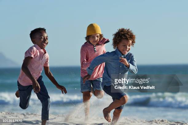 children running and laughing together on the beach - black shorts stockfoto's en -beelden