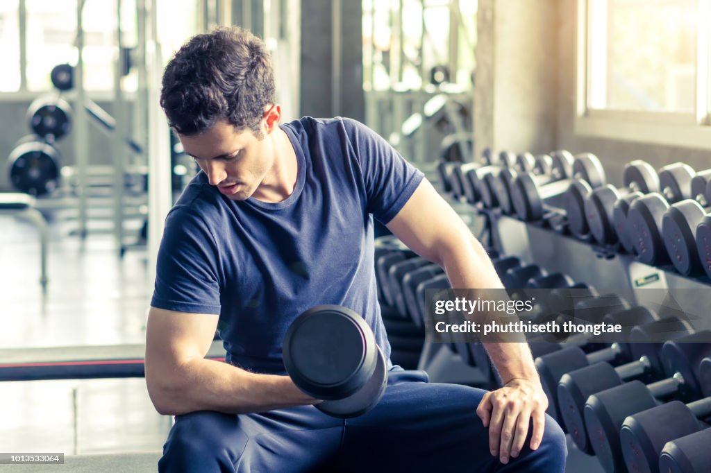 Fitness, sport, training and lifestyle concept - Young man with dumbbell flexing muscles in fitness gym center.